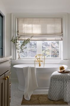 a white bath tub sitting under a window next to a rug on the side of a sink