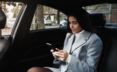 a woman sitting in the back seat of a car looking at her cell phone