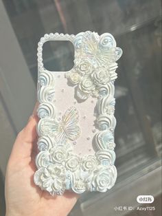 a hand holding up a phone case with flowers and butterflies on the back in front of a window