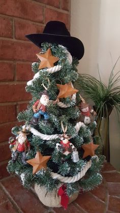 a small christmas tree decorated with ornaments and hats on it's head, sitting in front of a brick wall