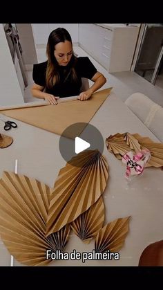 a woman sitting at a table working on some paper art work in front of her