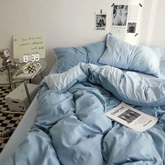 an unmade bed with blue comforter and pillows on it in a white room