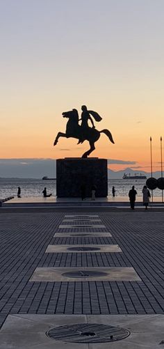 a statue of a man riding a horse in front of the ocean with people walking around