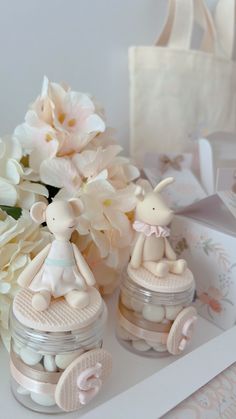 there are two small jars with little figurines in them and flowers on the table