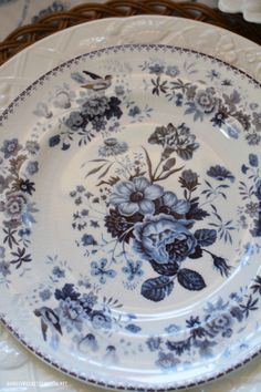 an ornate blue and white plate on a wicker tableclothed place setting with flowers