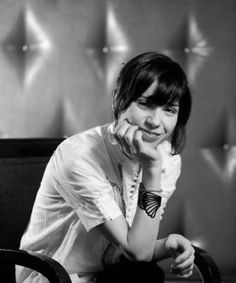 a woman sitting in a chair with her hand on her chin and looking at the camera