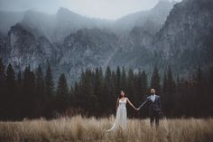 a bride and groom holding hands in front of mountains with trees on the other side