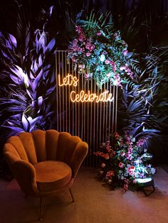 an orange chair sitting in front of a neon sign that says let's celebrate