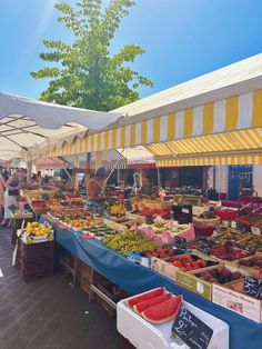 an outdoor market with lots of fruits and veggies on display under awnings