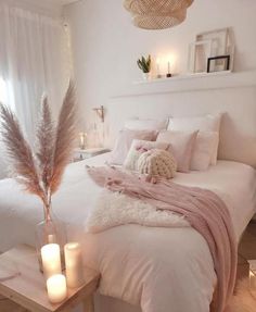 a white bed with pillows and blankets on top of it next to two lit candles