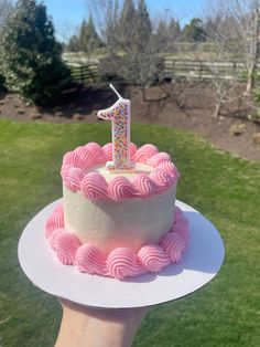 a pink and white cake with a one candle on top