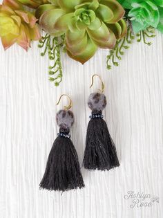 two black tasseled earrings hanging from hooks next to a succulent plant