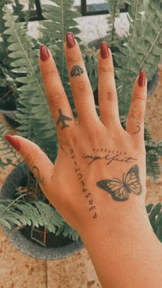 a woman's hand with tattoos on it and a plant in the back ground