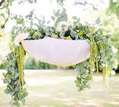 an arrangement of flowers and greenery is hanging from a tree in the park for a wedding ceremony