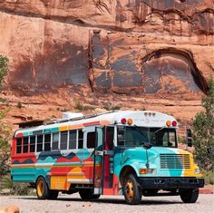 a colorful bus parked in front of a large rock formation with trees and bushes around it