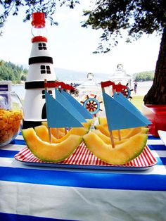 a table topped with watermelon boats and pineapples next to a lighthouse