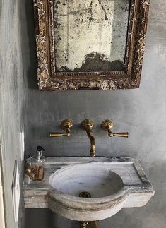 a bathroom sink sitting under a mirror next to a wall mounted faucet with gold fixtures