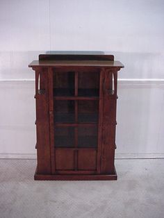 a small wooden cabinet with glass doors on the top and bottom, in front of a white wall