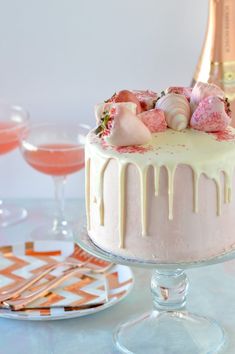 a cake with white icing and pink flowers on top, next to champagne glasses