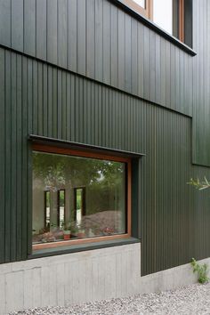 an empty bench in front of a green building with large windows and gravel area next to it