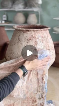 a woman is making a vase out of clay and wrapping it around with plastic wrap