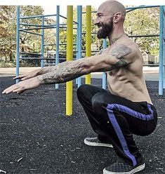 a man squatting on the ground in front of a playground with his arms stretched out