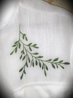 a close up of a white shirt with green leaves embroidered on the front and back