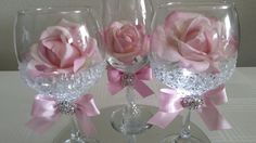 three wine glasses decorated with pink roses and diaper on a white tableclothed surface