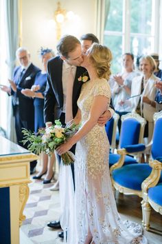 a bride and groom kissing in front of an audience at a wedding ceremony with blue chairs