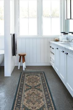 a bathroom with white walls and gray rugs on the floor, along with two windows