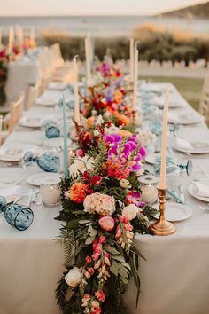 a long table with flowers and candles on it is set up for an outdoor dinner