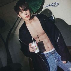 a shirtless young man holding a drink in his right hand and wearing ripped jeans