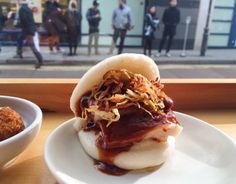 a sandwich with meat and sauce on a plate next to a bowl of fried food