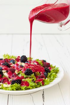 a white plate topped with salad covered in berries and dressing being drizzled over it