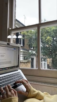 a person sitting in front of a window using a laptop computer with their hands on the keyboard