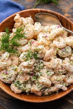 a wooden bowl filled with shrimp salad on top of a table next to a blue towel