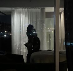 a woman standing in front of a window next to a night time scene with the lights on