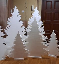 three white christmas trees sitting on top of a hard wood floor next to a door