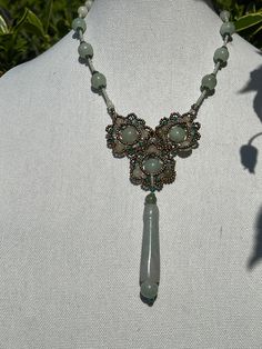 This beautifully executed necklace is made of stands are jade beads interspersed with glass beads for a visual effect. They connect in the front in a floral cluster and a jade medallion tops it off. This is a one of a kind, necklace and we think it is truly special. This floral inspired necklace from a husband and wife team that take beads, jade and present them in beautiful novel ways. It's handmade, and we procured the only one they had. Details: Button clasp. Size: Length of strand (from flow Elegant Jade Pendant Crystal Necklace, Handmade Jade Necklace With Flower Pendant, Handmade Jade Flower Pendant Necklace, Jade Beaded Necklaces With Gemstone Pendant, Elegant Jade Crystal Necklaces With Round Beads, Elegant Beaded Jade Crystal Necklaces, Elegant Beaded Jade Crystal Necklace, Elegant Jade Crystal Necklace With Round Beads, Beaded Jade Jewelry