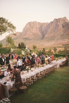 a large group of people sitting at long tables in the middle of a grassy field