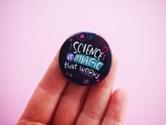 a hand holding a button that says science is magic that works