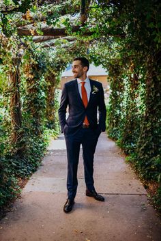 a man in a suit and tie is standing under an arch with greenery on it