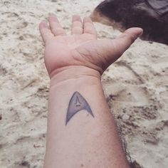 a person's arm with a small tattoo on it, and a star trek ship in the background