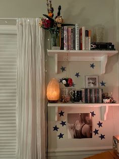 a shelf with books and pictures on it next to a window in a room that has white curtains