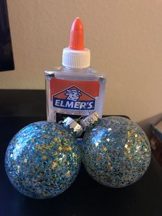 two glitter balls sitting on top of a table next to a glue bottle and an orange marker