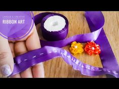 someone is holding a ribbon and some flowers on top of the purple ribbon with white dots