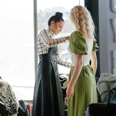 two women standing in front of a window with their hands on the back of their dresses