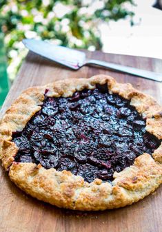 a blueberry pie sitting on top of a wooden cutting board next to a knife