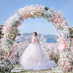 a woman in a white wedding dress standing under a floral arch with pink and white flowers