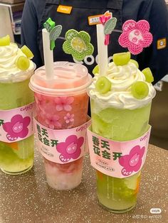 three cups filled with green and pink drinks on top of a table next to each other